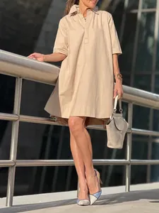 Robe chemise trapèze beige élégante et ample à manches courtes dans un cadre urbain.
