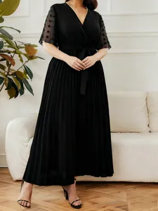 Elegant black V-neck pleated maxi dress with sheer polka dot sleeves in a living room setting