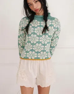 Close-up view of mint green floral jacquard knit sweater featuring a decorative yellow hem