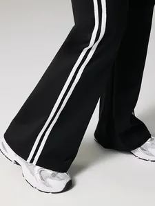 Schwarze Yoga-Schlaghose mit hoher Taille, zwei weißen Seitenstreifen und Sneakern