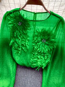 Detailed view of green chiffon top featuring 3D flower appliques and sheer fabric texture