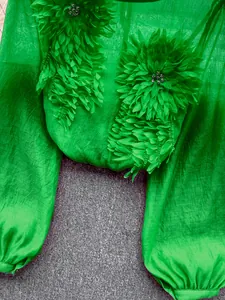 Close-up of green sheer chiffon blouse with 3D floral appliqués and lantern sleeves.