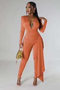 Full-length studio shot of a sexy orange deep V-neck long sleeve jumpsuit with side drape