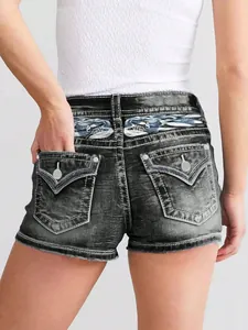 Detalle posterior de pantalones cortos vaqueros con bordados azules y bolsillos.