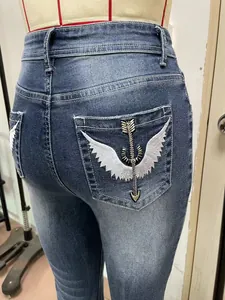 Macro detail shot showing heavy embroidery wing and arrow design on denim jeans back pocket.