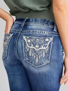 Dettaglio del ricamo floreale bianco sulla tasca posteriore dei jeans a zampa blu