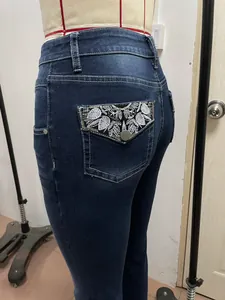Dettaglio macro dei ricami a foglia argentata sulla tasca posteriore dei jeans blu