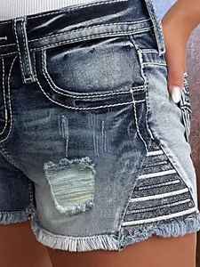 Detailopname van gescheurde denim shorts met borduursels en rafelige zoom.