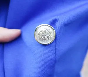Detailansicht eines silbernen Wappenknopfes an einem eleganten königsblauen Damenblazer.