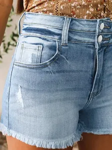 Détail de short en jean taille haute avec ourlets effilochés et fermeture à double bouton.