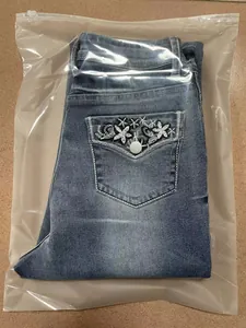 Detail view of blue denim jeans with white floral embroidery on the back pocket.