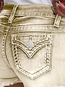 Detail van de achterzak van een denim short met decoratieve stiksels en metalen knoop.
