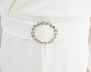 Detail view of an elegant rhinestone flower buckle on a white slim fit bodysuit