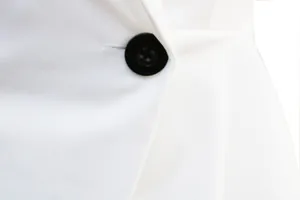 Nahaufnahme eines schwarzen Knopfes an einem weißen Blazerkleid mit feiner Textur