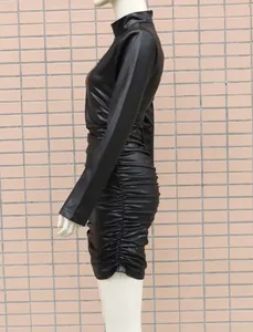 Détail des fronces latérales sur une mini robe moulante noire en similicuir à manches.