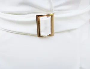 Detalle de cerca de un vestido blanco elegante con hebilla de cinturón rectangular dorada.