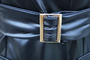 Detailansicht eines schwarzen Kunstlederkleides mit goldener Gürtelschnalle und Textur.
