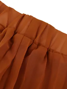 Close-up detail of pleated fabric and elastic waistband on caramel wide-leg trousers