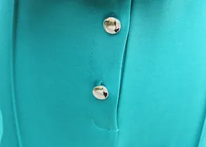 Macro detail showing the teal fabric texture and shiny silver buttons on elegant jumpsuit