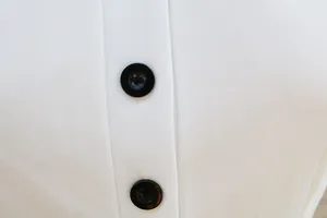 Dettaglio dei bottoni neri su un elegante abito aderente bianco a maniche lunghe