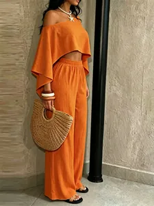 Primer plano de conjunto vacacional naranja de dos piezas con top asimétrico para playa.