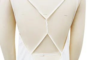 Detalle de vestido de playa blanco con tirantes cruzados y diseño trenzado atrás.