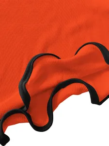 Close-up detail of orange rib-knit dress featuring a black wavy lettuce hem trim