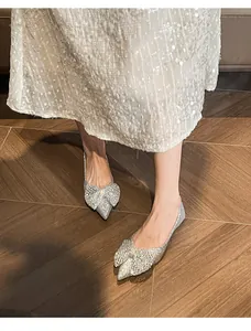 Close-up of silver sequin flat shoes with large bow on pointed toe worn by model