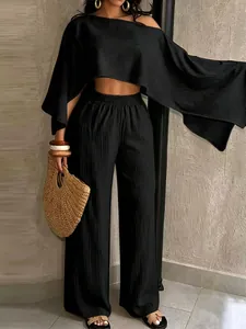 Detalle de conjunto negro de top asimétrico y pantalón ancho con textura plisada