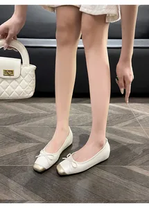 Detailed view of cream ballet flats with gold toe and bow detail on a model.