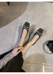 Top view of black ballet flats with rhinestone bow-tie detailing on gray tile floor