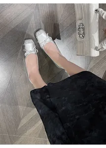 Elegant silver French style ballet flats with bow detail worn on wooden floor with white bag.