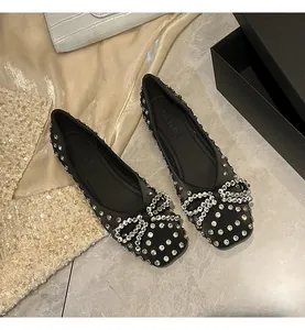 Close-up detail of black flat shoes with intricate rhinestone bow and stud patterns.