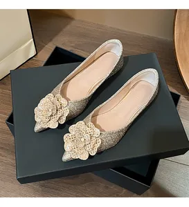Glittery gold pointed-toe flat wedding shoes with flower detail displayed on shoe box