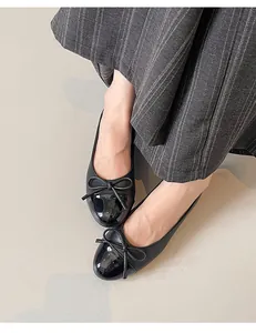 Detail view of elegant black ballet flats with bow and glossy toe cap on a person
