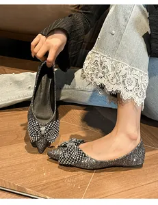Close-up detail of silver glitter pointed-toe flat shoes featuring a sparkling rhinestone bow