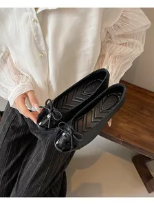 Detailed view of chic black ballet flats featuring a patent leather toe and bow accent