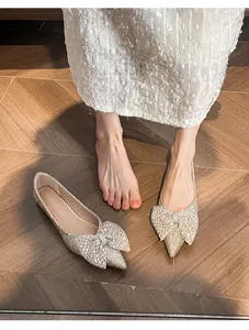 Elegant gold glitter pointed flats with a large bow detail shown on a wood floor