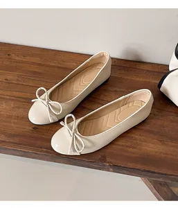 Angled detail shot of cream French style ballet flats with dainty bow accents on wood.