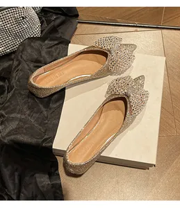 Close-up of golden sequined flat shoes featuring a large sparkling rhinestone bow