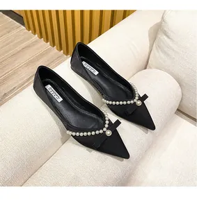 Detail view of black pointed-toe flat shoes with elegant pearl and bow decorations.