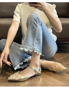 Champagne gold pointed-toe flat sandals with rhinestone flower embellishment worn by a model.