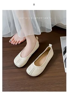 Eleganti ballerine bianco panna con punta a finta divisione su pavimento in legno scuro