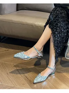 Detail view of elegant silver rhinestone flat sandals with ankle strap on model's feet