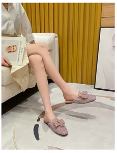 Detail view of sparkly rhinestone flat mules with bow decoration on a model's feet