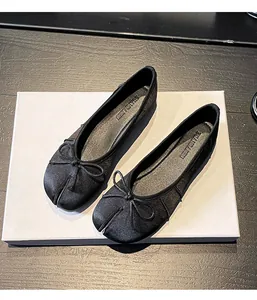 Detail view of stylish black split-toe ballet flats featuring a chic bow on a white board