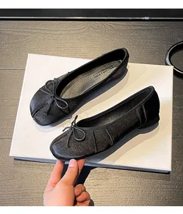 Close-up of black Tabi split-toe ballet flats with bow detail on white box.