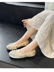 Ballerines champagne élégantes avec fleurs en strass et nœud portées par un mannequin.