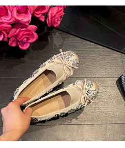 Gros plan de ballerines en satin champagne avec fleurs en strass et détail de nœud.