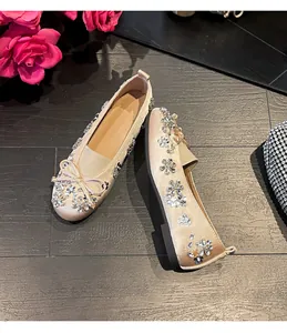 Ballerines champagne élégantes avec fleurs en strass et nœud sur un sol en bois sombre
